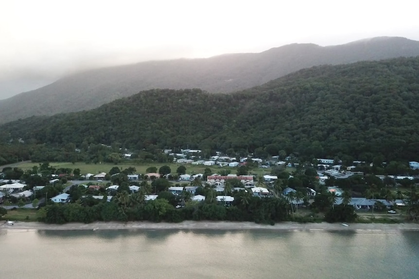 A drone of the community of Yarrabah, with row houses near the water and green hills in the background.