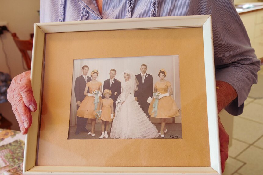 A woman holds an old photo of a wedding party.
