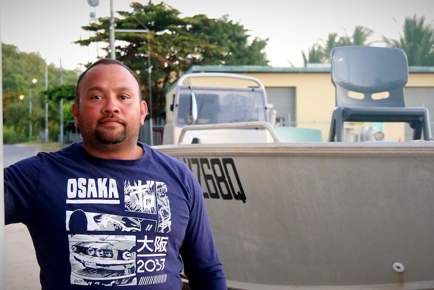 a man stands next to a petrol bowser with his boat in the background 