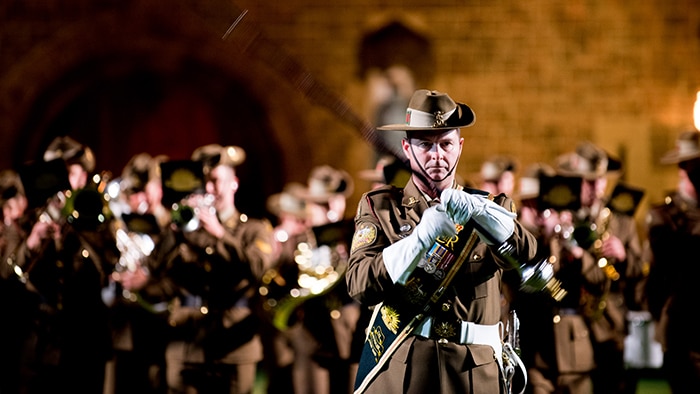 A military marching bang perform in brown uniforms.