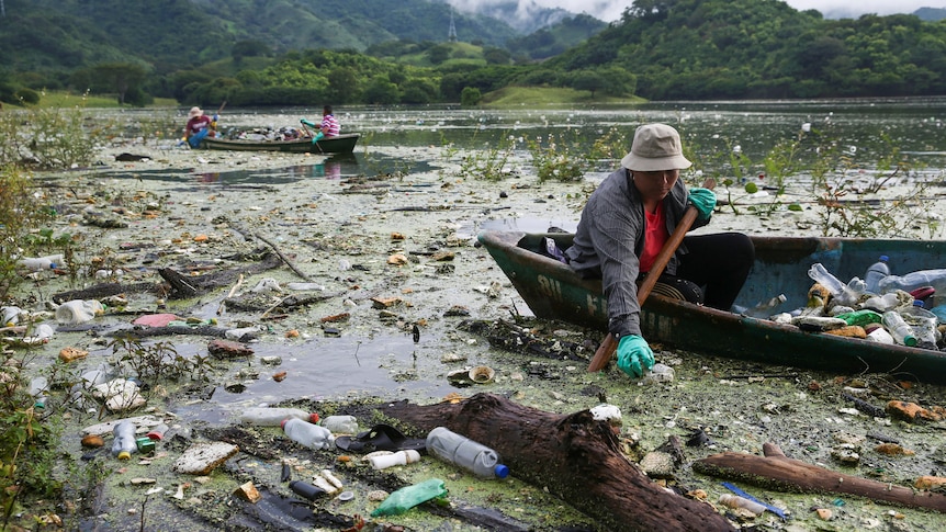 people in boats take rubbish out of a lake which is covered in trash