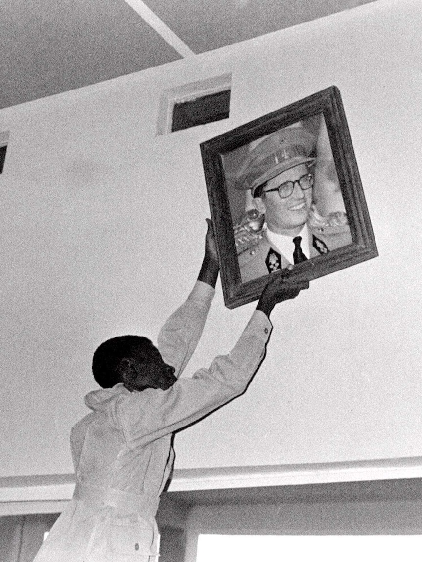 An unidentified Congolese citizen removes a portrait of Belgium's King Baudouin in this black and white photo from 1966.