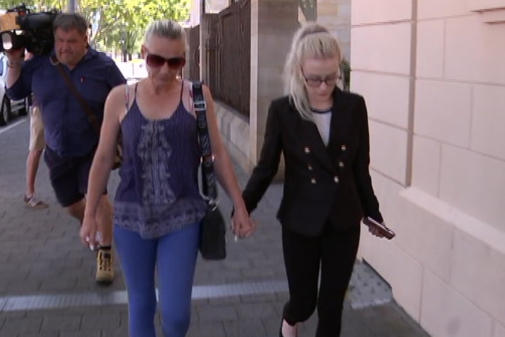 Two blonde women holdings hands in a city street with camera operators nearby