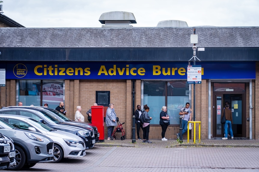 A line of people waiting outside a building that says Citizens Advice Bureau on it.