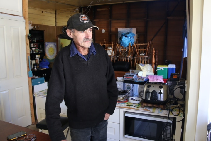 Paul Cotton wears a cap and a black fleece with jeans in his small kitchen