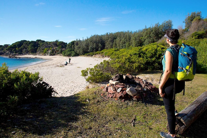 A girl looks out at the turquoise waters and white sand of Mowarry Beach from a campsite.