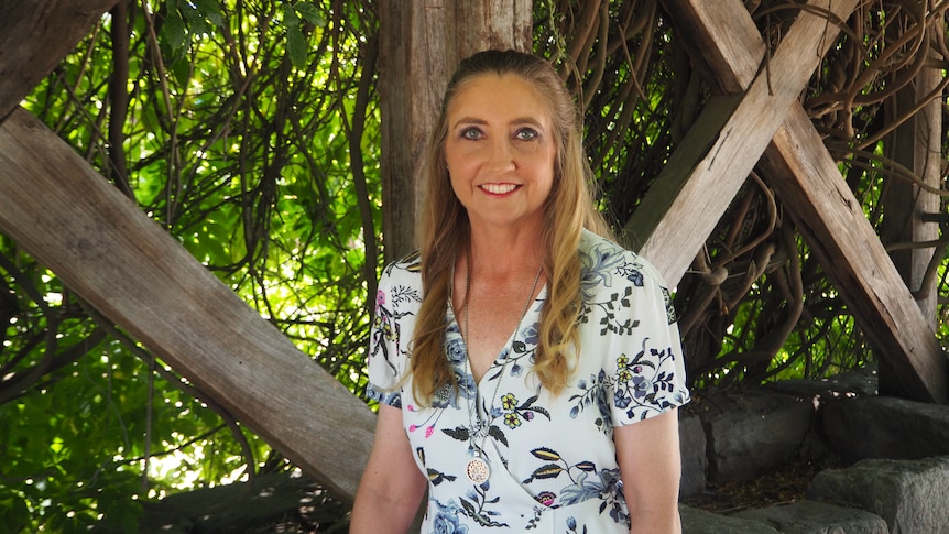 A middle-aged woman stands in a garden patio smiling.