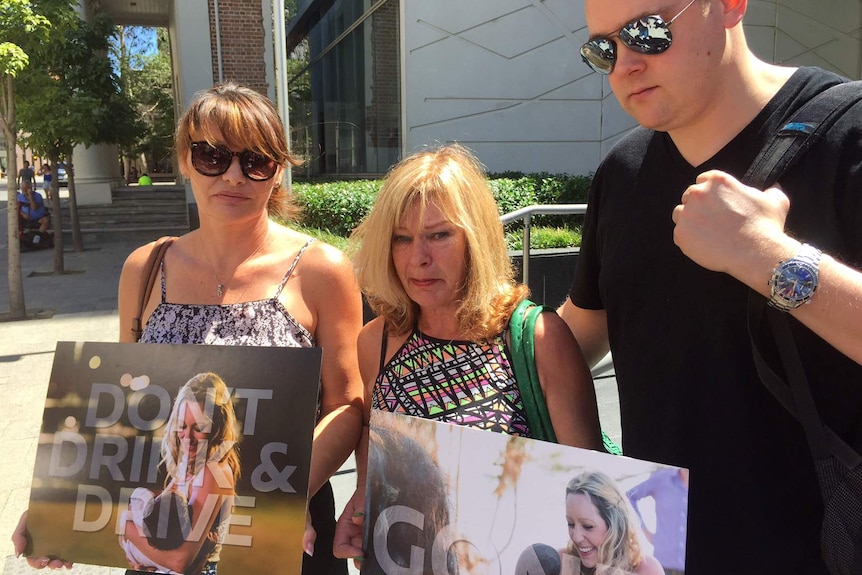 Two women and a man stand outside a Perth court holding placards with a woman's face and a message, 'Don't drink and drive'.