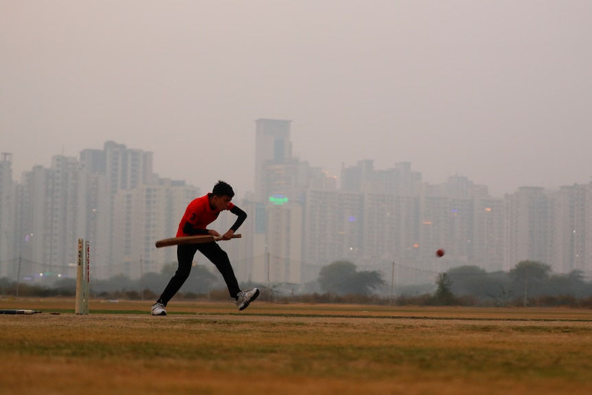 A boy plays cricket amidst smog at a playground.