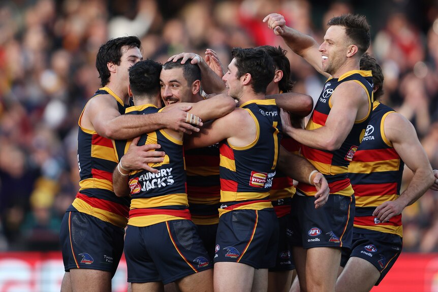 A group of Adelaide Crows men's players crowd around the full-forward to congratulate him after a goal.