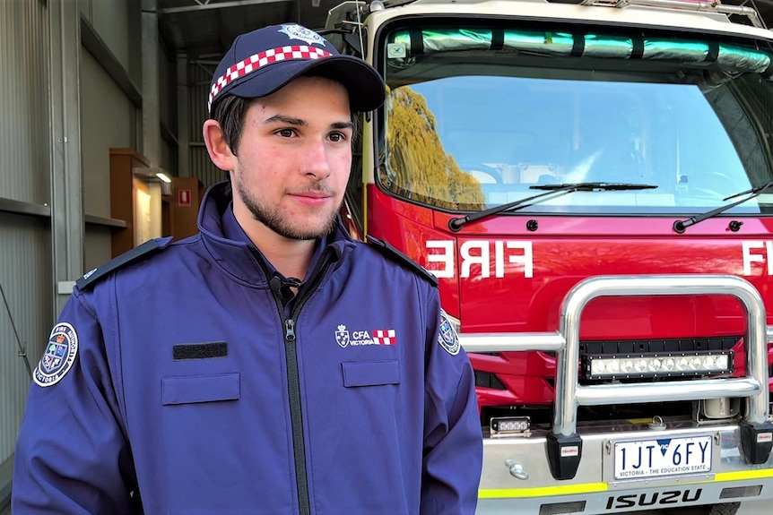 A teenager wearing a navy fire coat in front of a fire truck 
