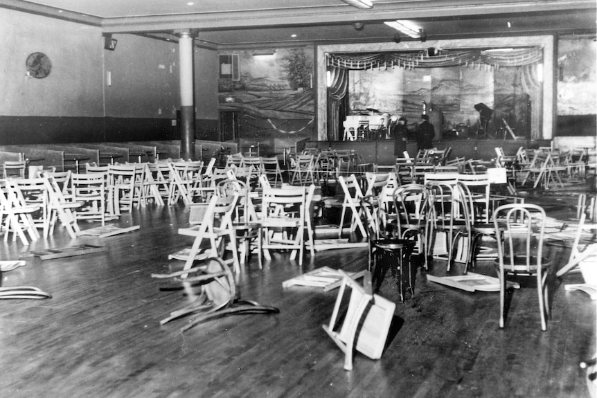 Черно-белое фото бального зала с перевернутыми стульями.