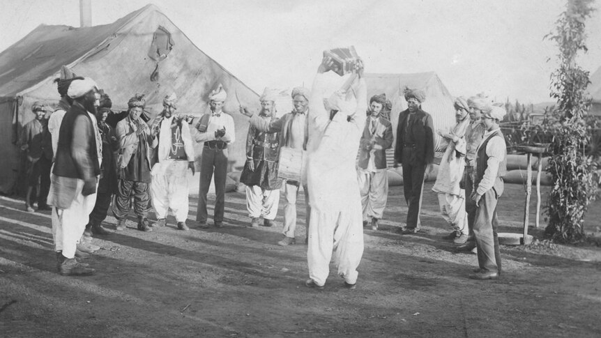 14 Afghan men in traditional outfits and turbans smiling and dancing in the 1890s