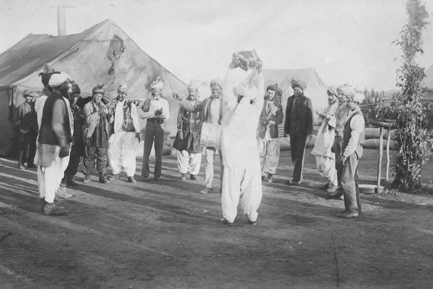 14 Afghan men in traditional outfits and turbans smiling and dancing in the 1890s