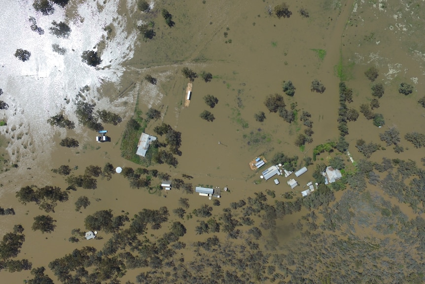 Drone image shows a bird's eye view of a house completely surrounded by floodwater