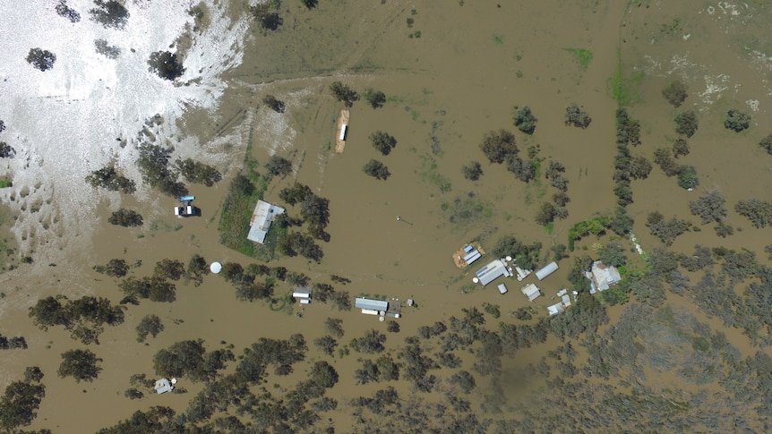 Drone image shows a bird's eye view of a house completely surrounded by floodwater
