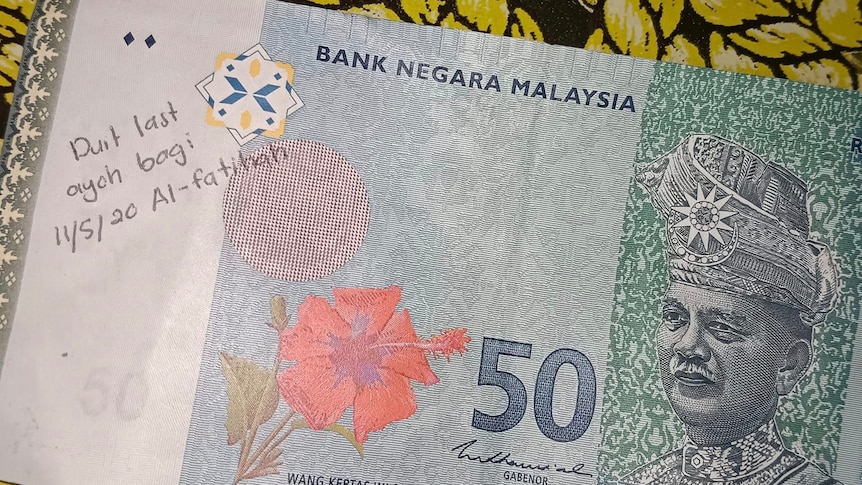 A Malaysian 50 ringgit banknote with a handwritten message on left-hand side in Malay
