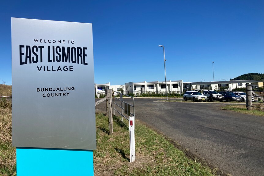 sign East Lismore Village, with pod housing visible in the background