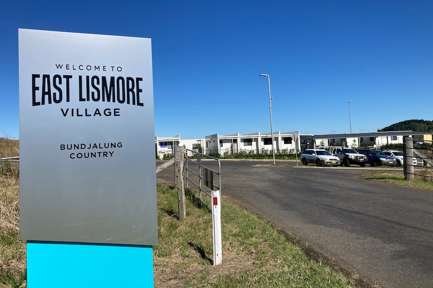 sign East Lismore Village, with pod housing visible in the background