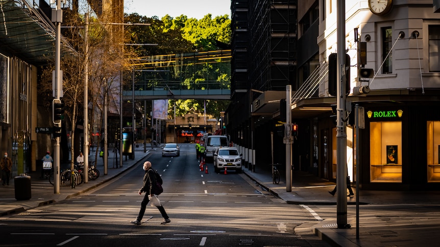 a man in a mask crossing a mostly empty road