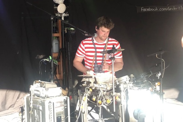 A young man in a stripy shirt plays a drumkit.