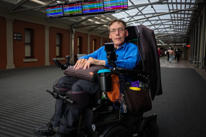 Peter Tully, who uses a wheelchair, wears a blue button up shirt at a train station.