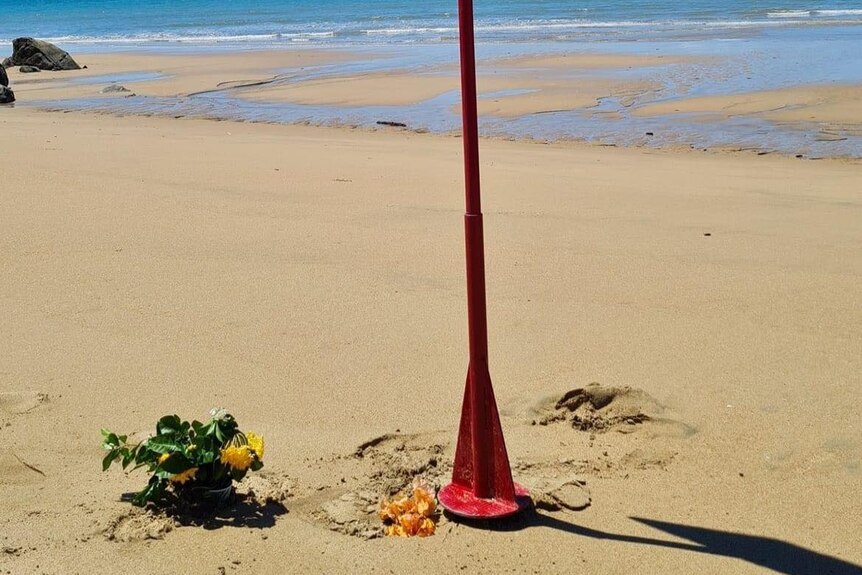 A small group of flowers left on the sand at the base of a sign