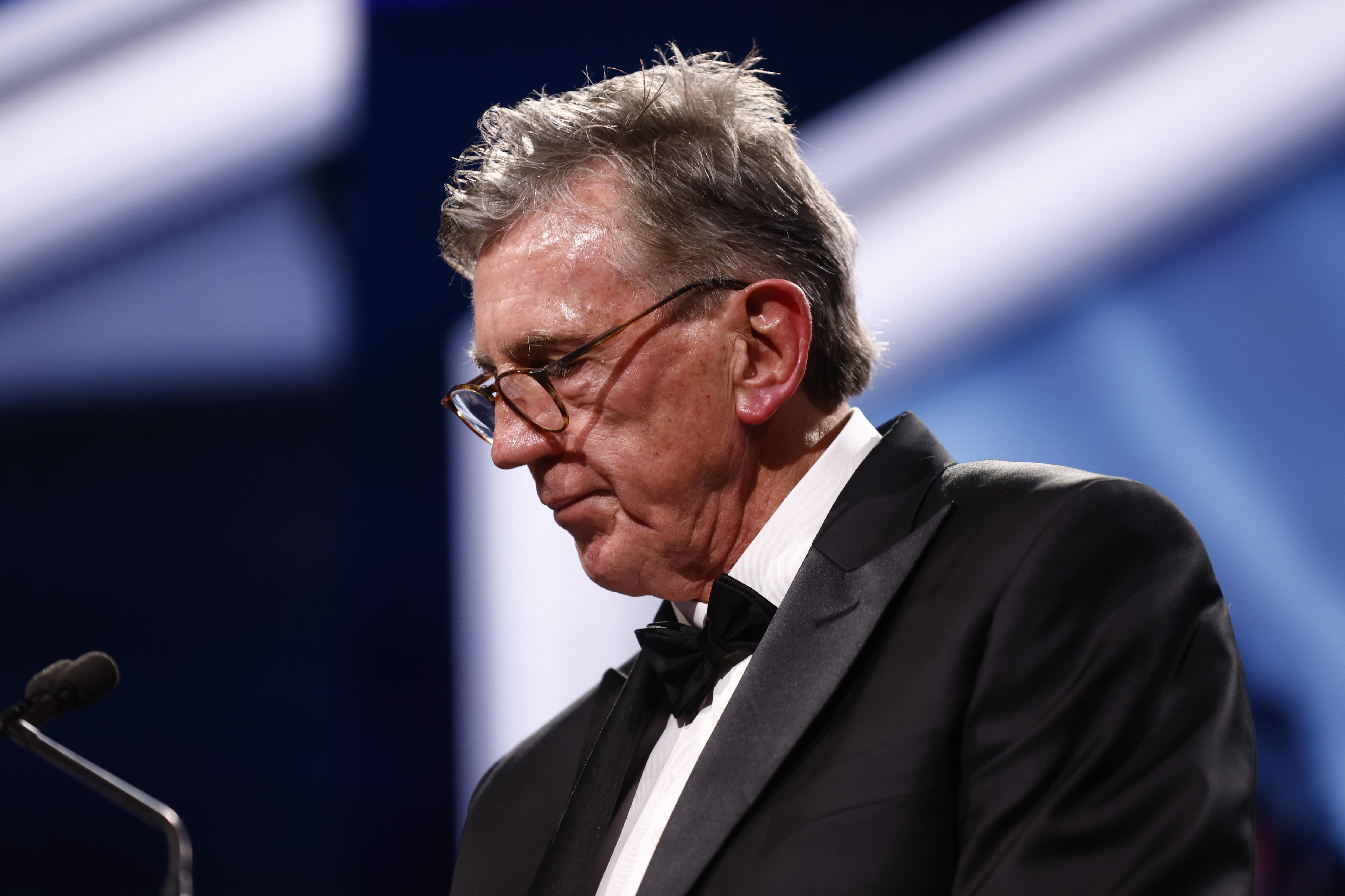 An older man wearing glasses and a tuxedo and standing at a lectern.
