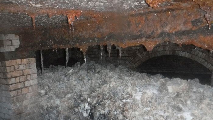 A grey and white mass of congealed fats and household items blocks two thirds of an old brick sewer.