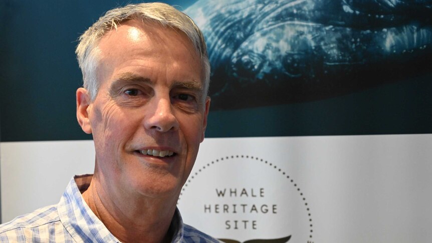 Fraser Coast Tourism general manager Martin Simons stands smiling infront of a whale sign.