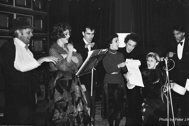 black and white image of actors speaking / singing into microphones in costume