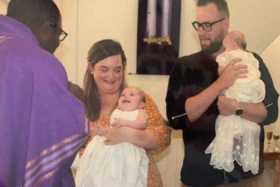 Twins being christened and held in arms of their parents