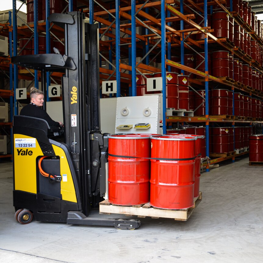 There are four red drums on a pallet, being lifted by a yellow and black forklift.
