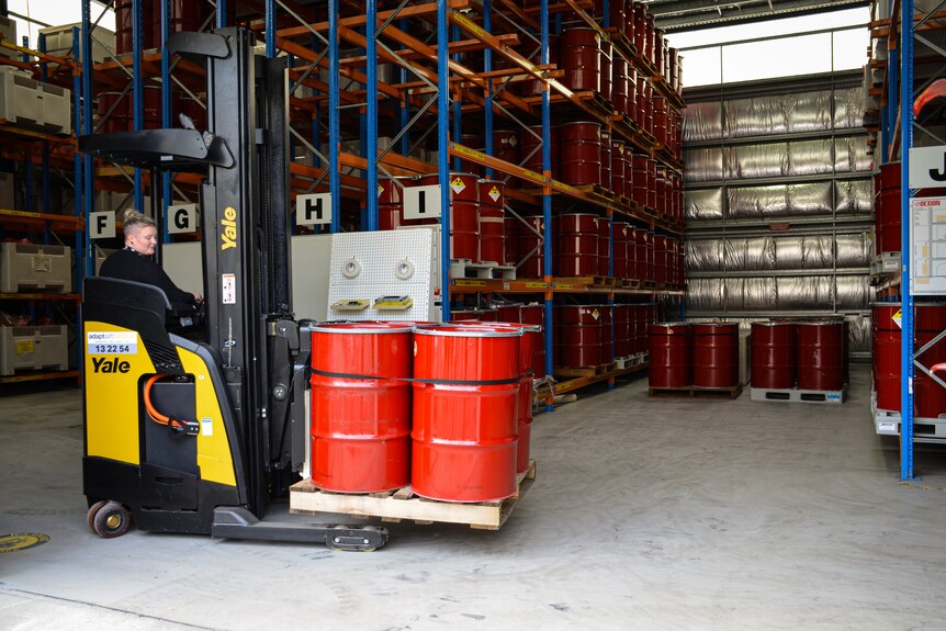 There are four red drums on a pallet, being lifted by a yellow and black forklift.