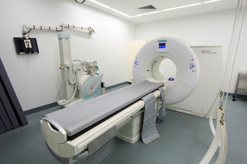 A CT scanner, a bit white donut shaped machine with a bed that can go inside the hole. In a clinical white room