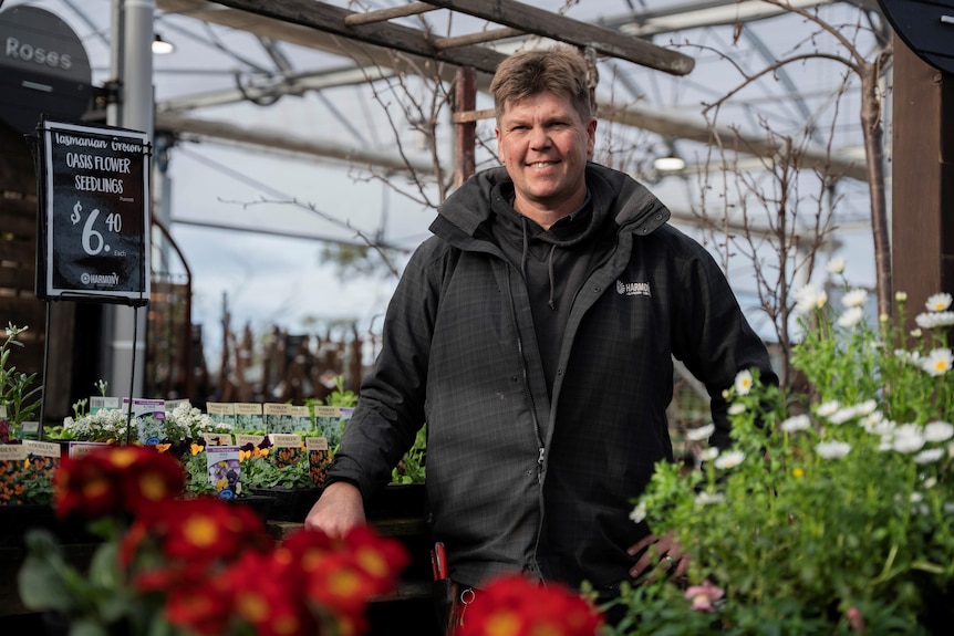 A man wearing a warm jacket stands in front of seedlings in a garden nursery.