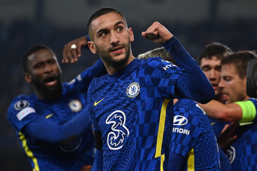 Hakim Ziyech clenches his fist and looks up as Chelsea players hug behind him