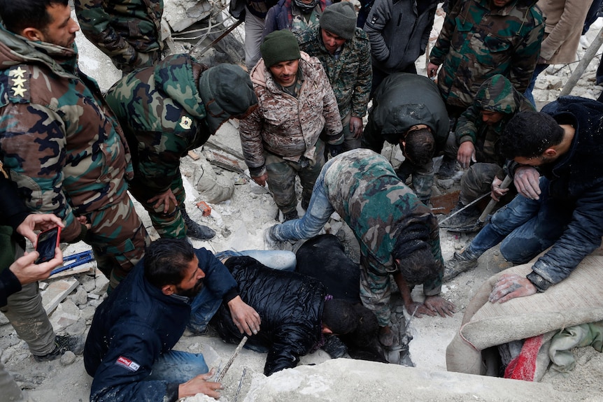 Men in uniform stand in a circle with some on the groiund working to rescue people. 