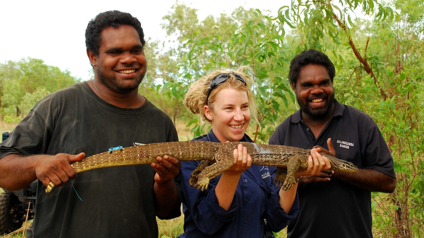 Three people hold up a goanna smiling