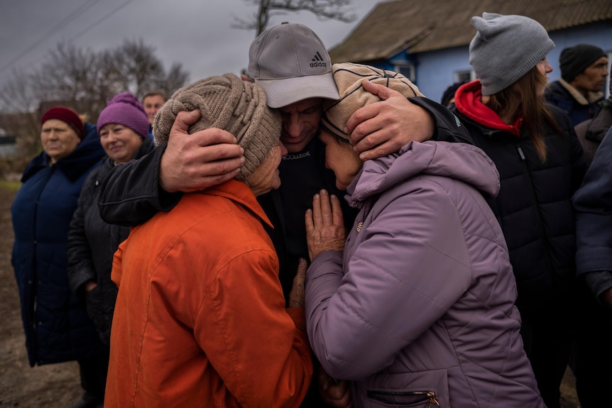 Three people embrace with their heads held together. 