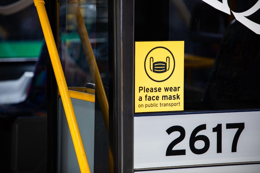 A yellow sign on a bus window reading 'Please wear a mask on public transport'.