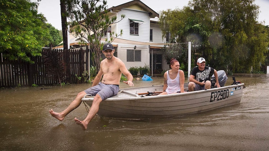 Residents Stephen Jubbs, Stacie Little and Stephen Dobbs take their boat around floodwaters in Rosslea in Townsville,.