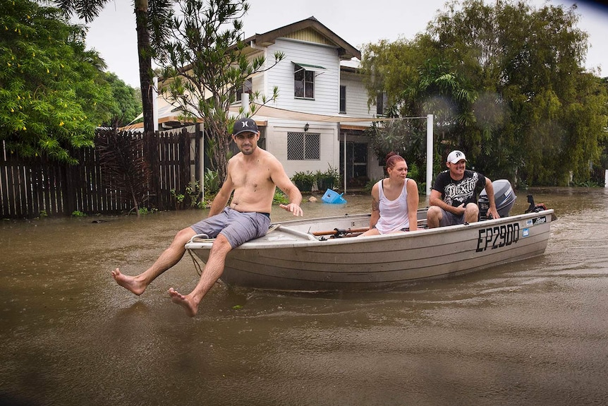 Residents Stephen Jubbs, Stacie Little and Stephen Dobbs take their boat around floodwaters in Rosslea in Townsville,.