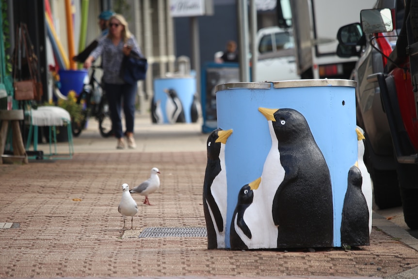 A rubbish bin on a pathway with artwork of painted penguins
