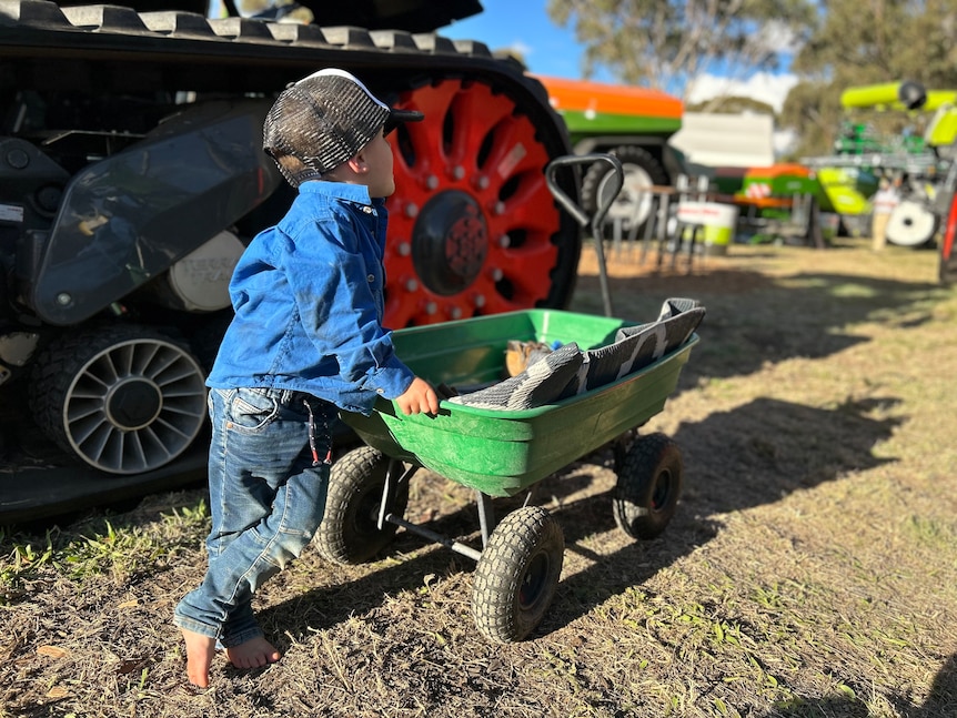a young boy leans against a trolley next to a large tractor