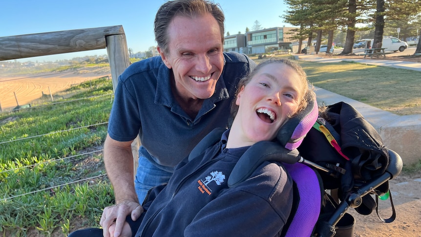A man bends down and smiles next to young woman in a wheelchair