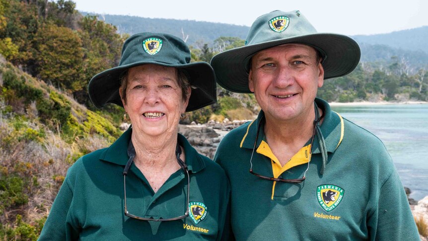 Picture of a woman and a man in green uniforms wearing hats with water and trees in the background