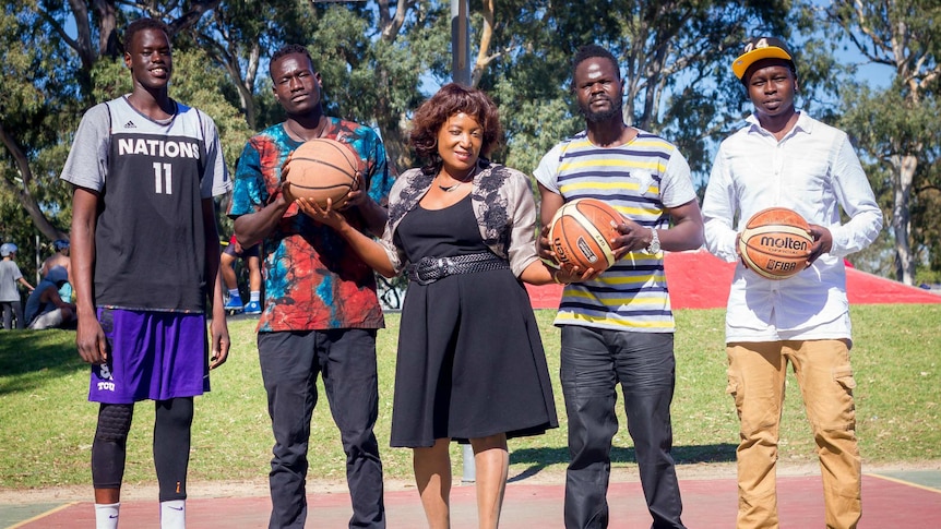 Four basketball players stand with a woman holding two basketballs.