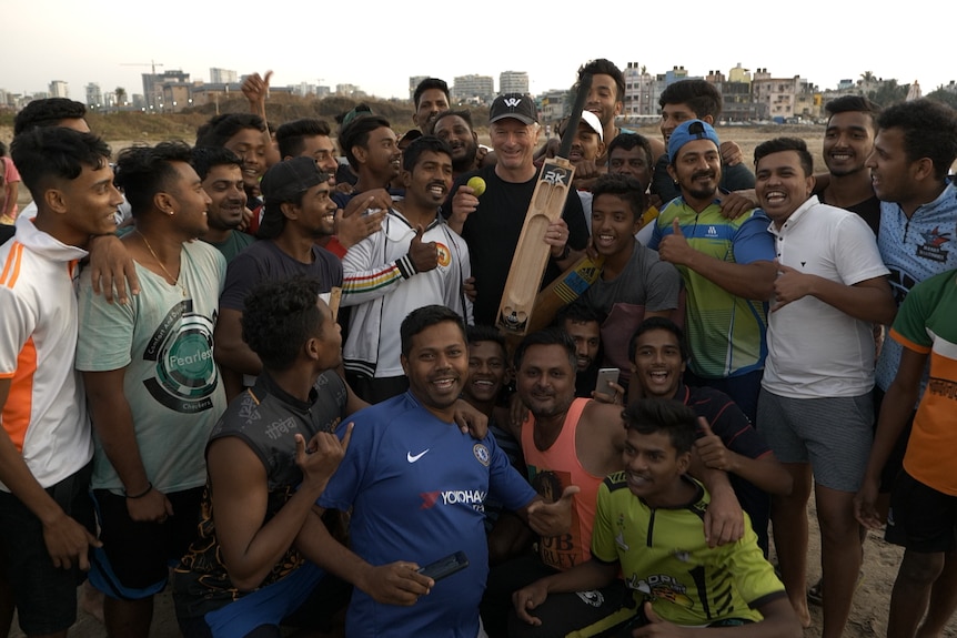 Waugh holding bat and ball surrounded by large crowd of men.