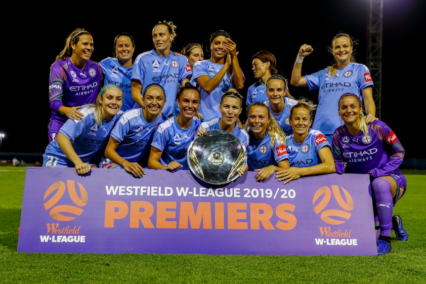 Soccer players wearing blue stand behind a sign after they won a competition